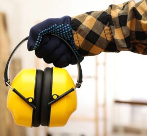A hand wearing a work glove, holding a pair of yellow over the ear ear muffs for hearing protection
